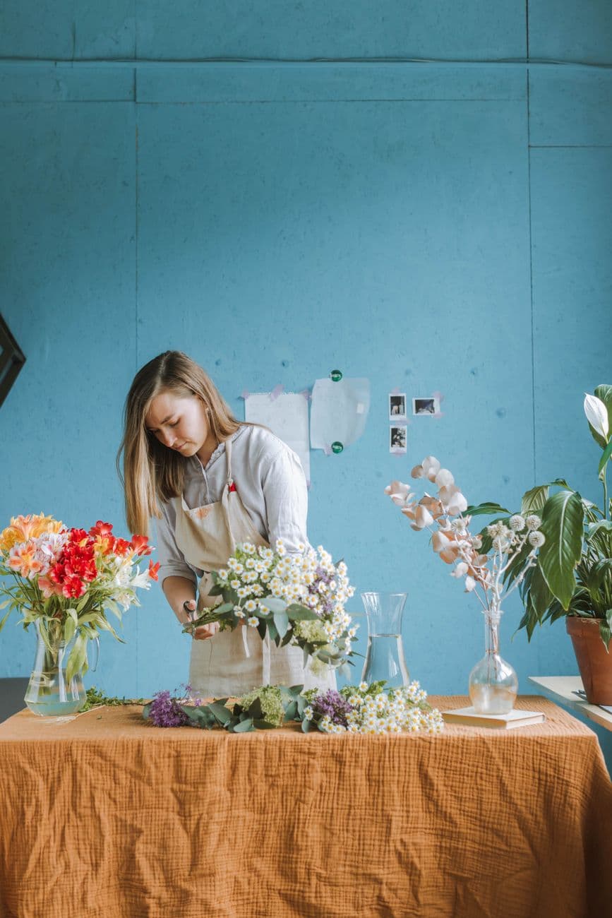 A florist arranges colorful flowers on a table in a bright indoor workshop.