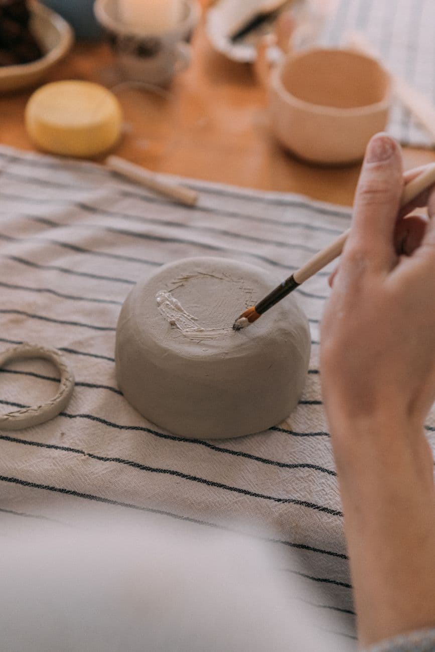Detailed close-up of an artisan hand-painting a handcrafted clay bowl, showcasing artistic craftsmanship.
