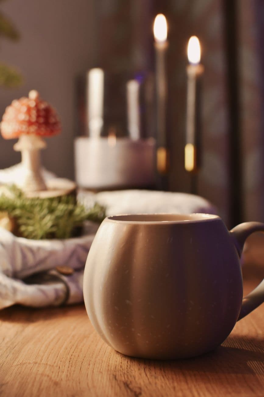 A warm mug set against a backdrop of lit candles and rustic winter decor creates a cozy ambiance.