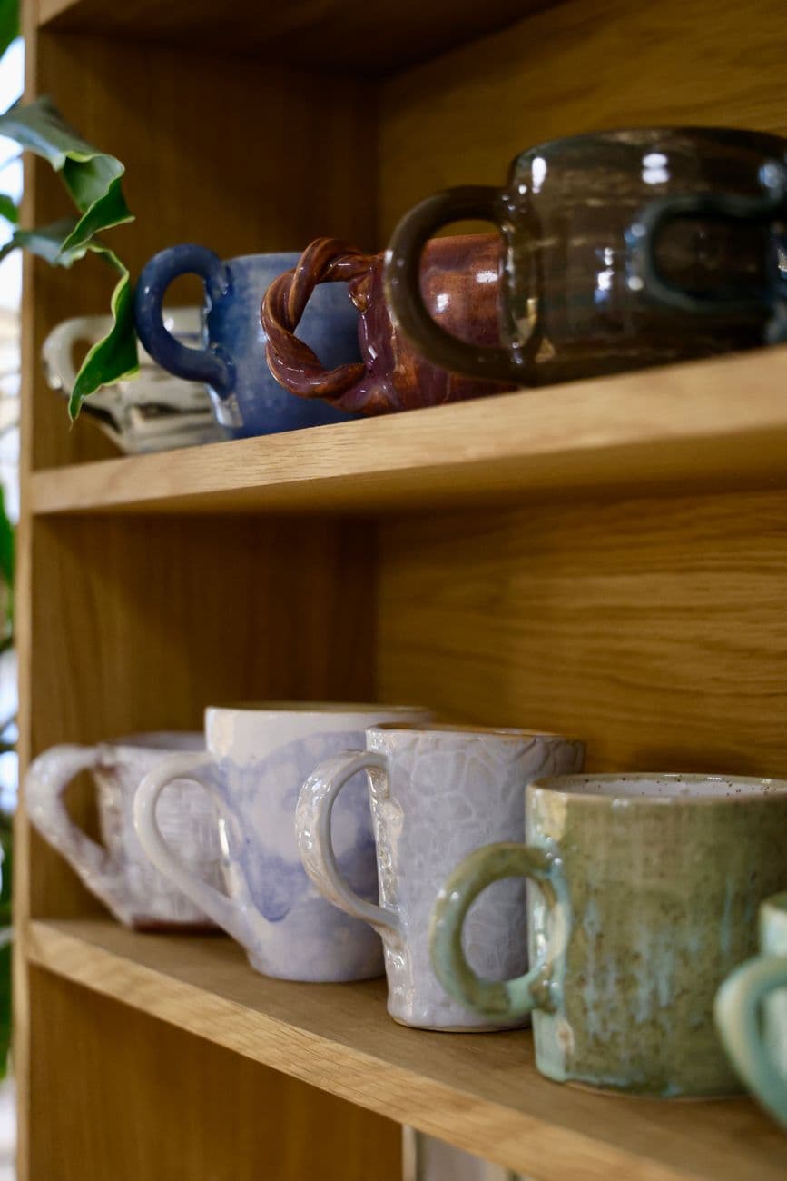 A collection of handcrafted ceramic mugs arranged on wooden shelves, offering a rustic and artistic touch.