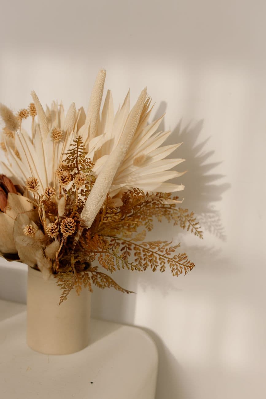 Stylish dried floral arrangement in a ceramic vase against a white wall in soft natural light.
