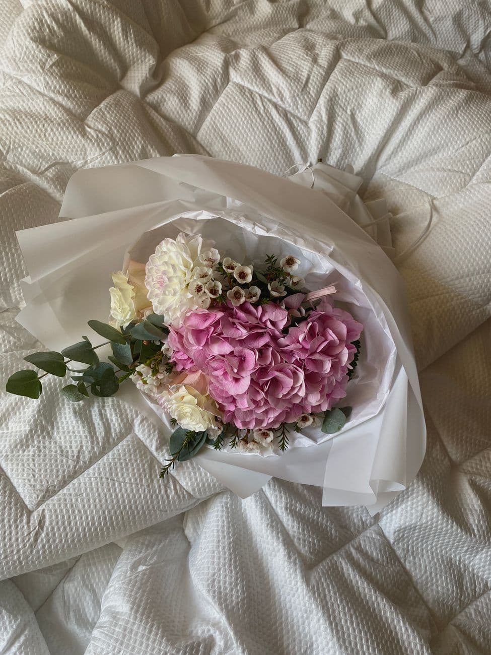Luxurious bouquet of pink and white flowers beautifully arranged on a soft white duvet, showcasing elegance and serenity.