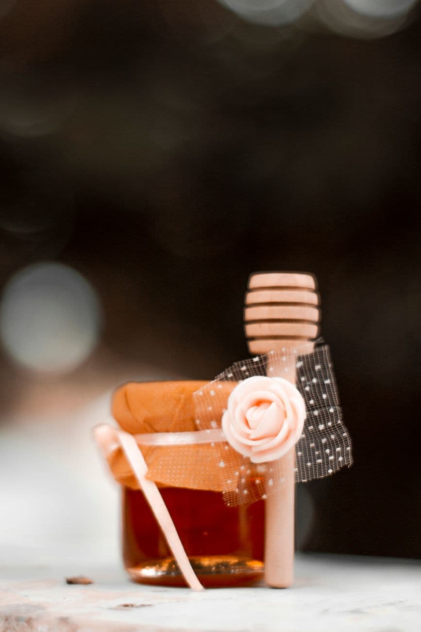 Stylish jar of honey adorned with a flower and decorative stick, perfect for gourmet presentation.