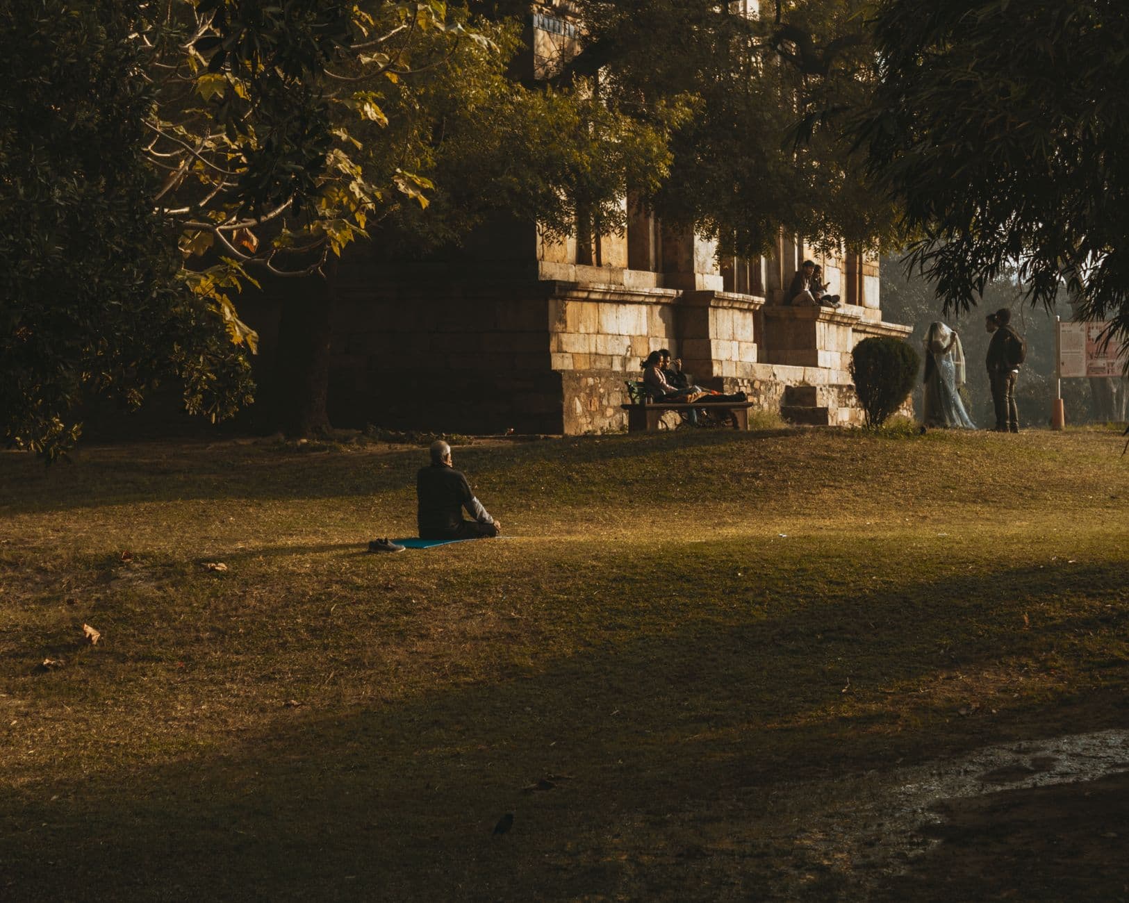 A person meditates on a mat in a tranquil park amidst historical architecture, capturing peace and relaxation.