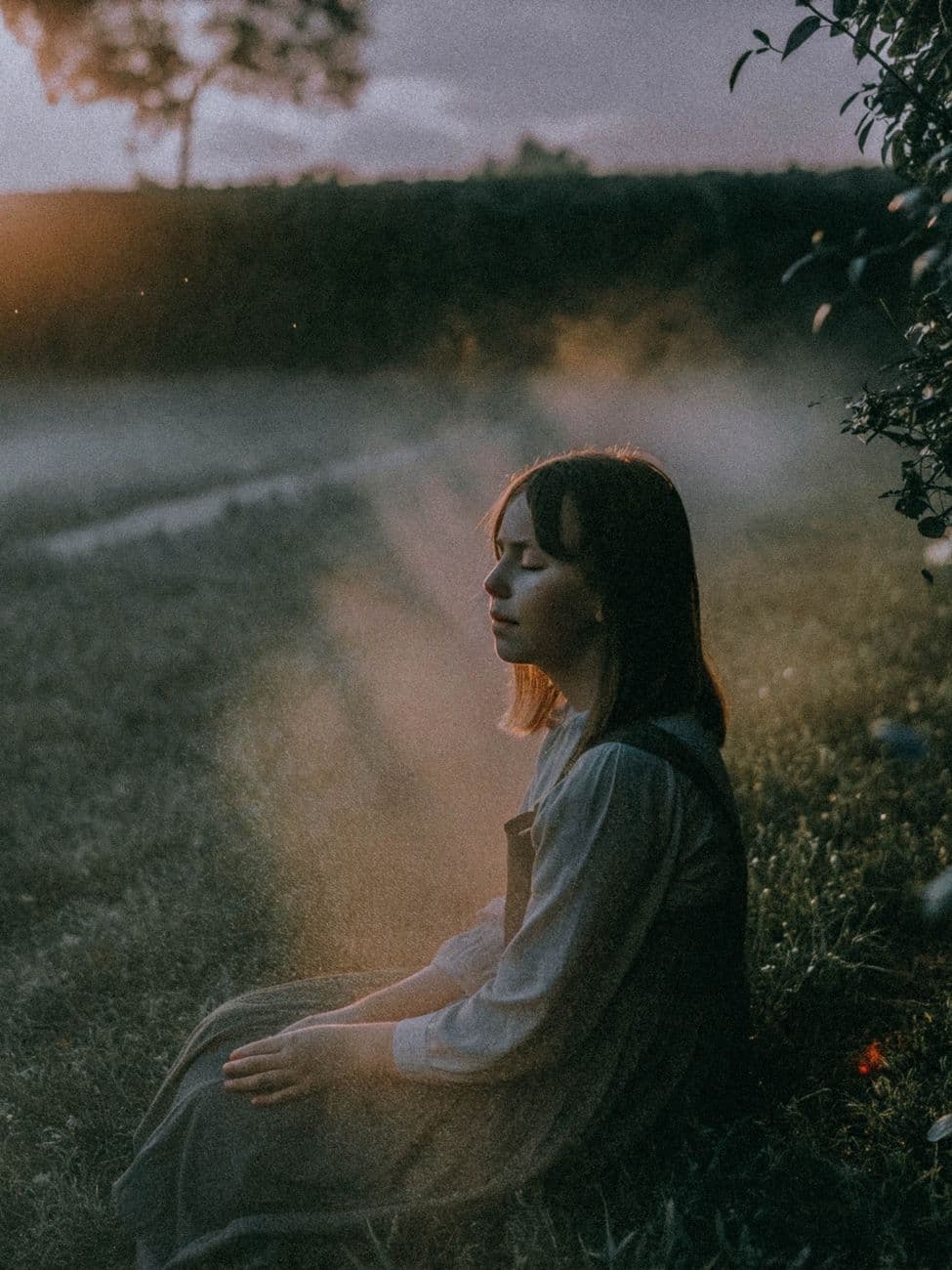 Silhouette of a woman meditating in a misty field at sunset.